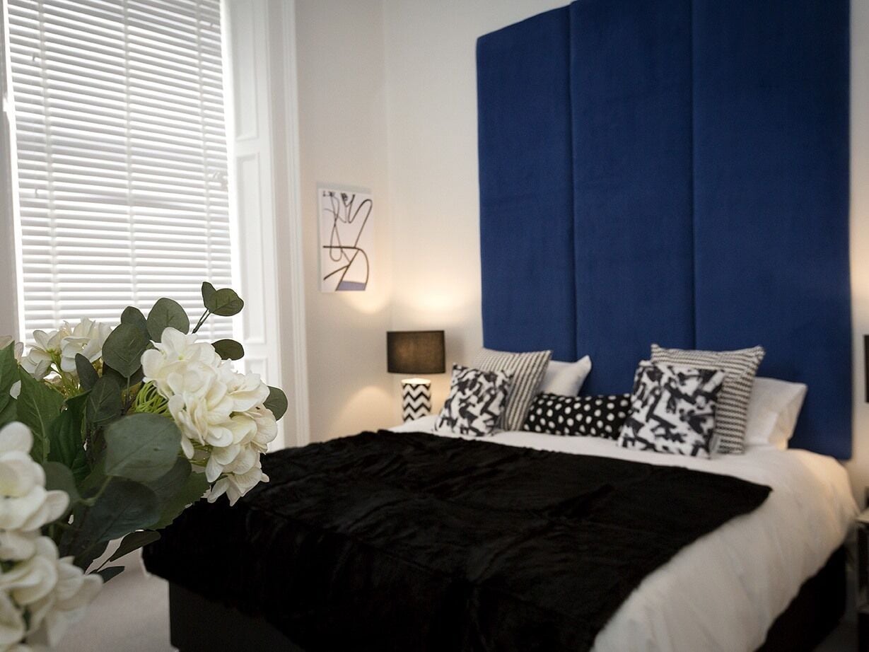 A bedroom with a large bed, a blue headboard, and a bedside table with a lamp.