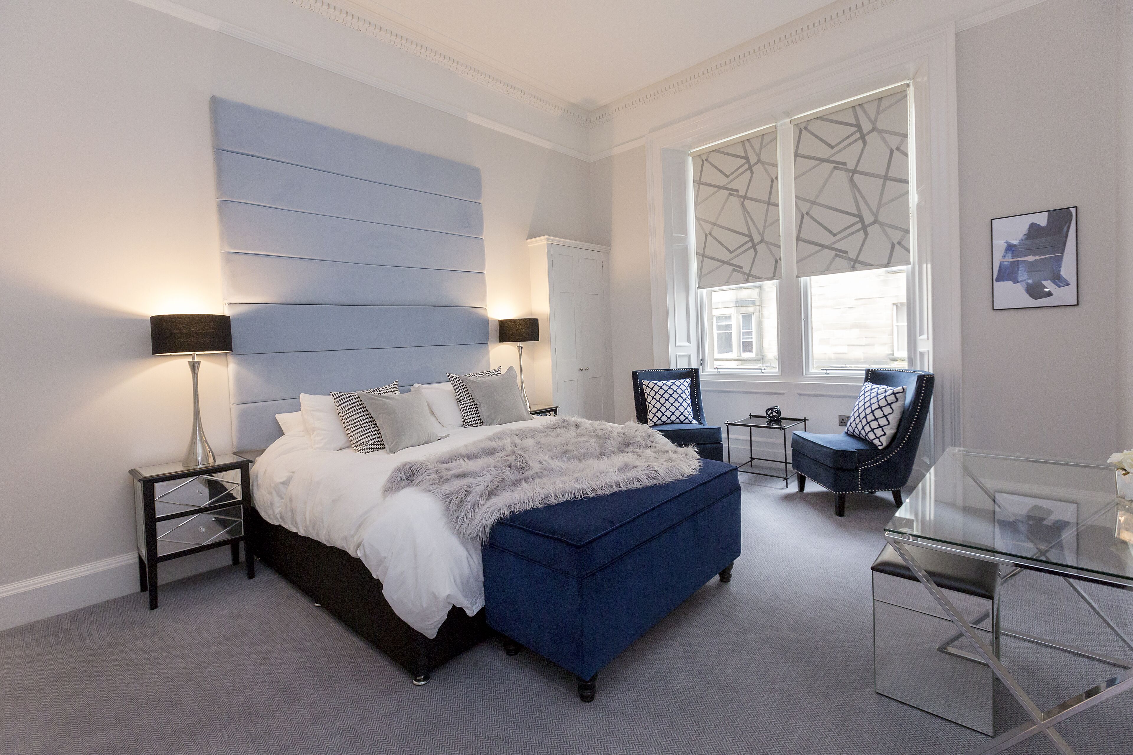 A modern bedroom with a large bed, a glass coffee table, and a view of the city through large windows.