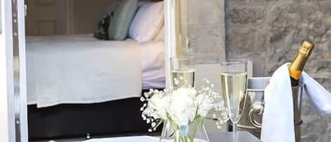 A room with a bed, a table with a vase of flowers, and a bottle of champagne.