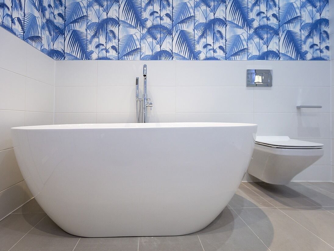 Een moderne badkamer met een vrijstaand bad, toilet en een wandmengkraan.