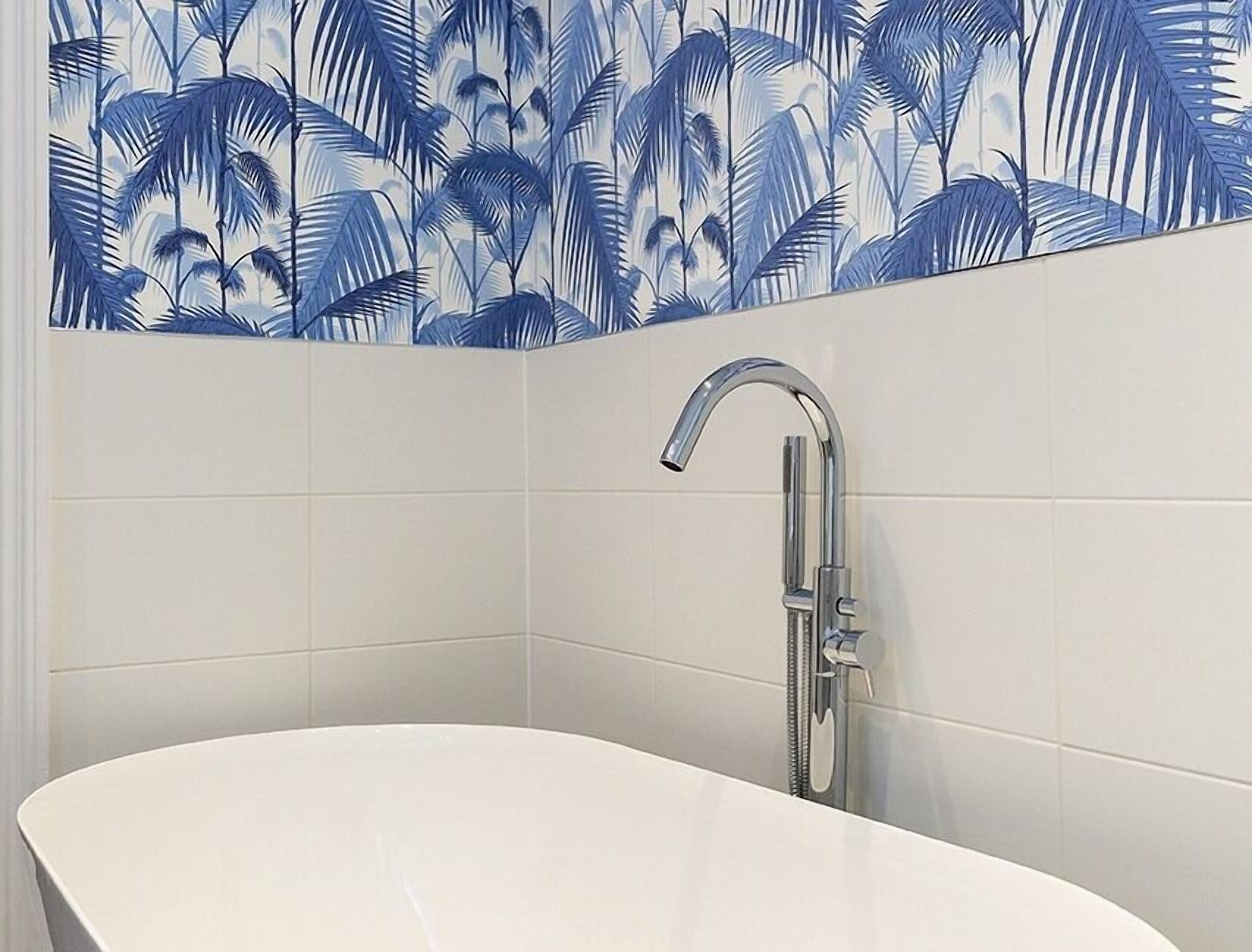 A bathroom with a white bathtub, a chrome faucet, and a wall with a blue palm leaf pattern.