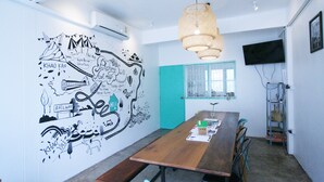 A conference room with a long wooden table, chairs, a map mural on the wall, a teal door, and a hanging light fixture. - Hello Hostel Pakchong (Pak Chong)