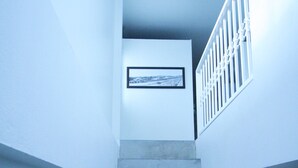 A staircase with a white railing, a framed picture on the wall, and a window with blinds. - Hello Hostel Pakchong (Pak Chong)