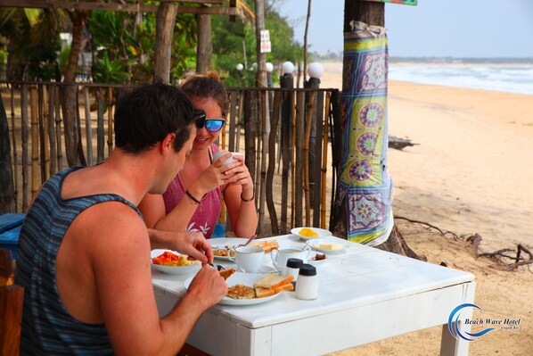 A beachside dining area with a table set for two, featuring a variety of dishes and a cup of coffee. - Beach Wave Hotel (Arugam Bay)
