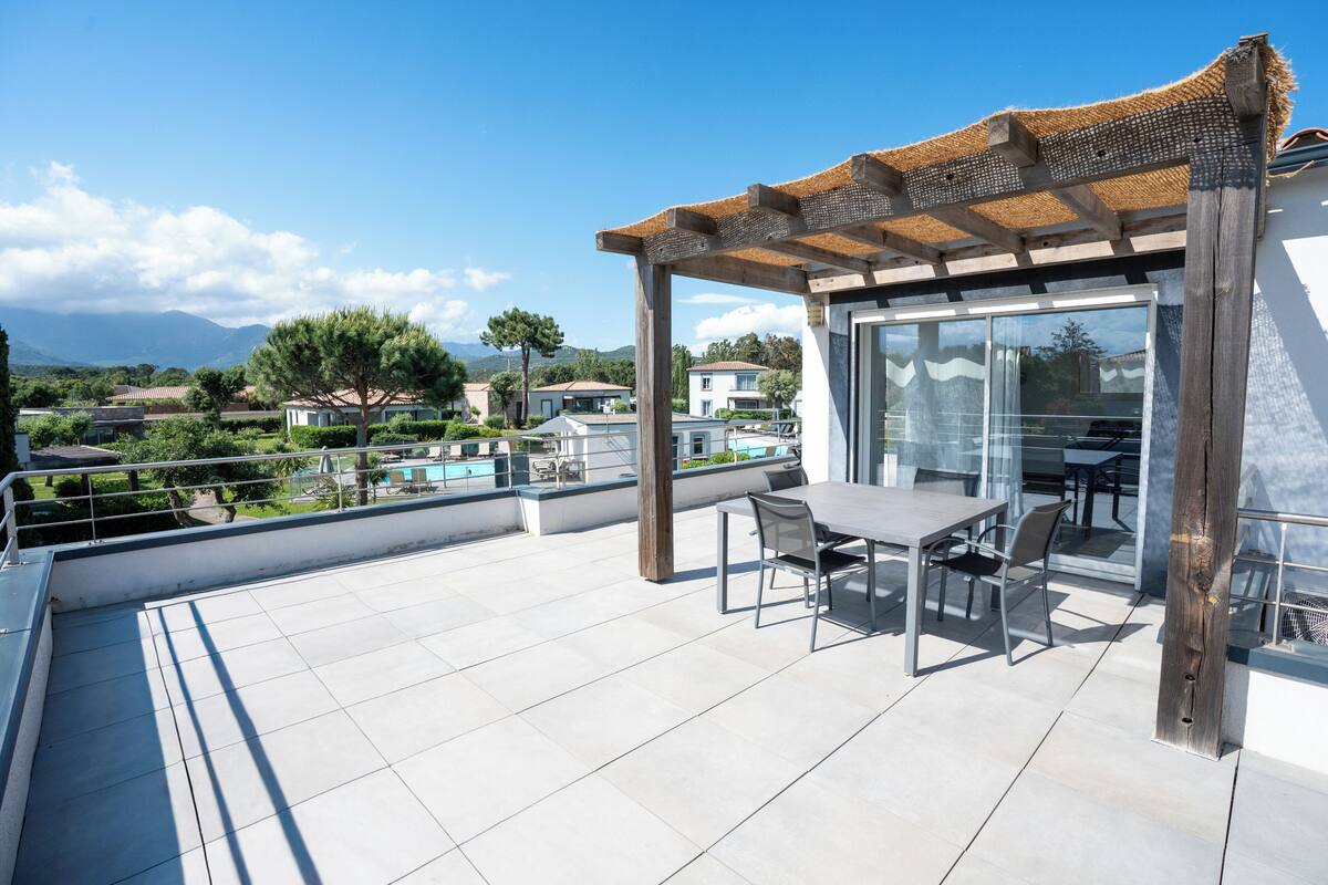 A rooftop terrace with a pergola, glass sliding doors, and a dining table with chairs.