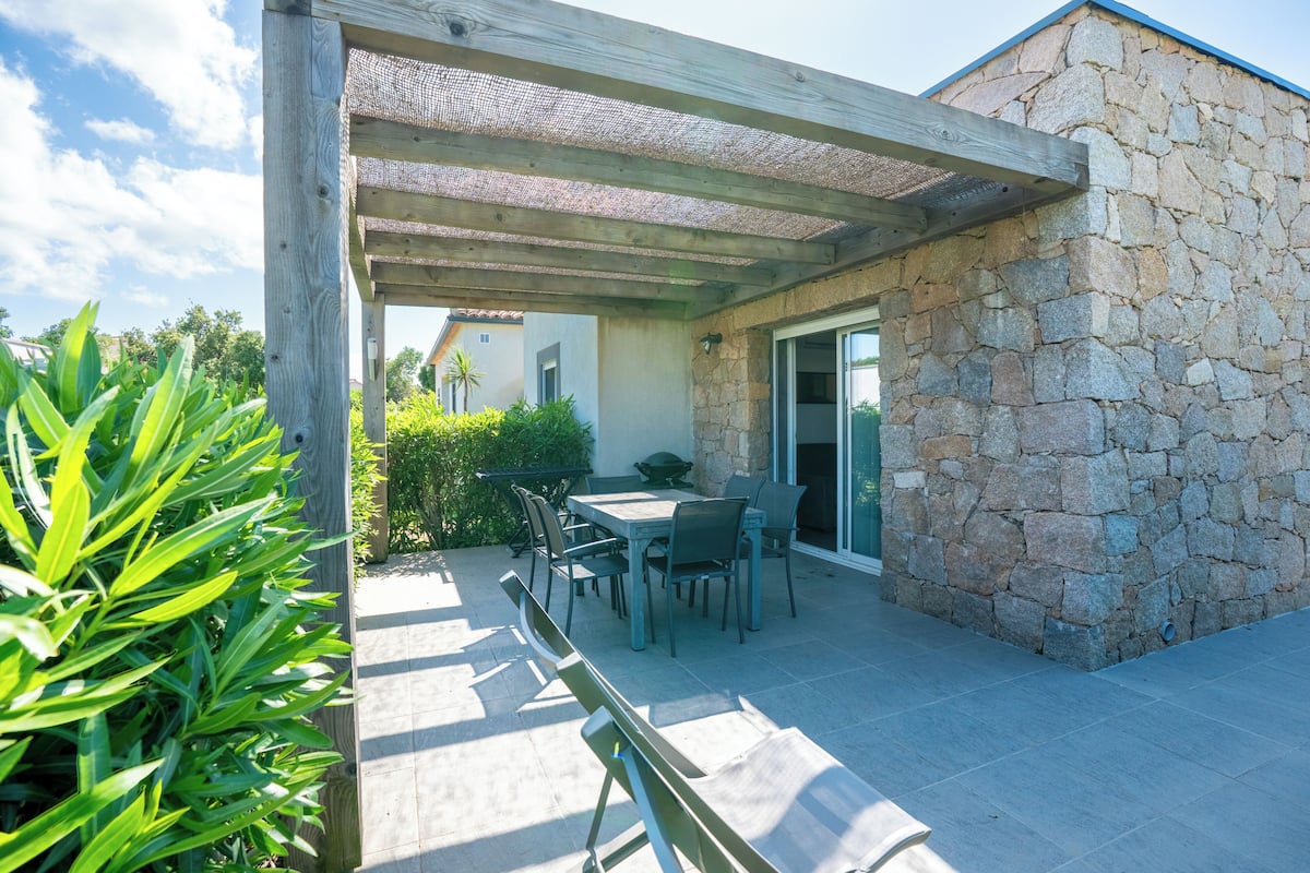 An outdoor patio with a stone wall, a wooden pergola, and a table with chairs.