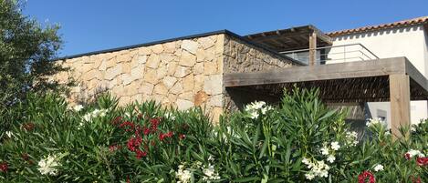 A stone building with a wooden pergola and flowering plants in front.