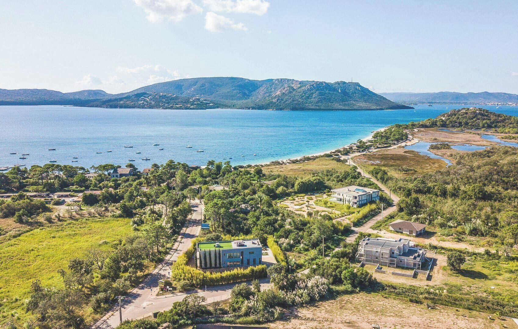 Ett flygbildsfoto av en fastighet vid kusten med flera byggnader, en väg och en vattenyta.