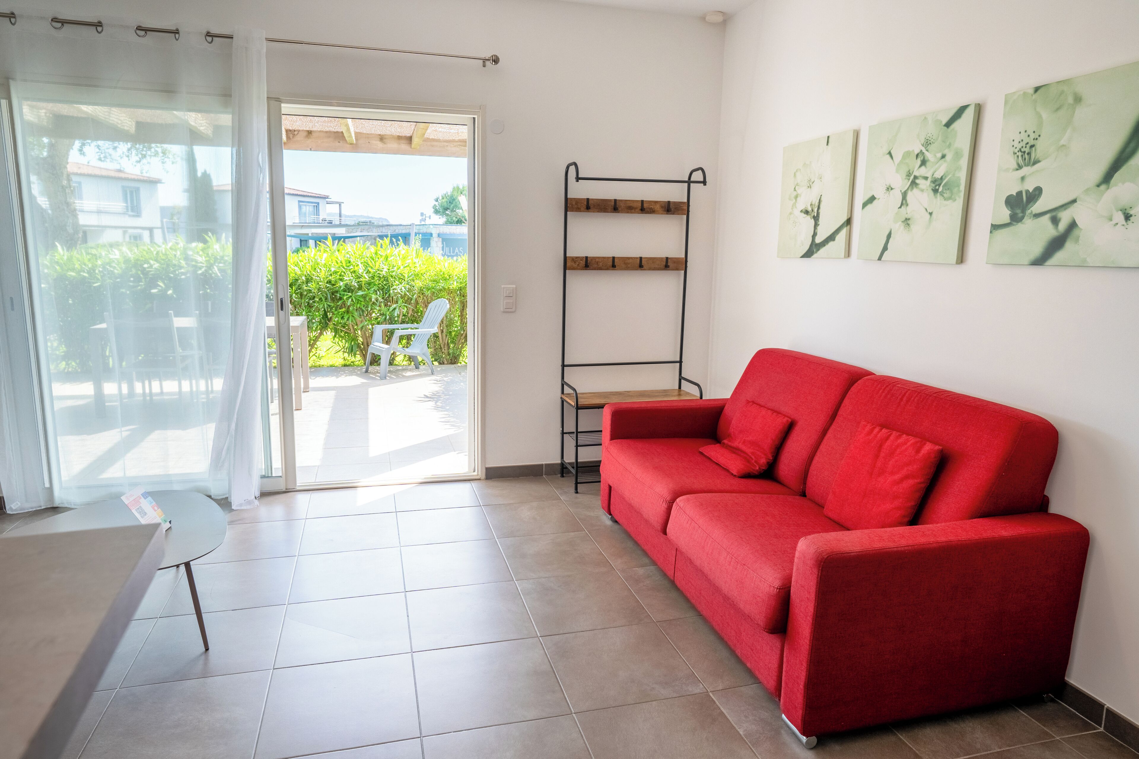 A red sofa, a small table, a metal rack, and a door leading to a balcony with a chair.