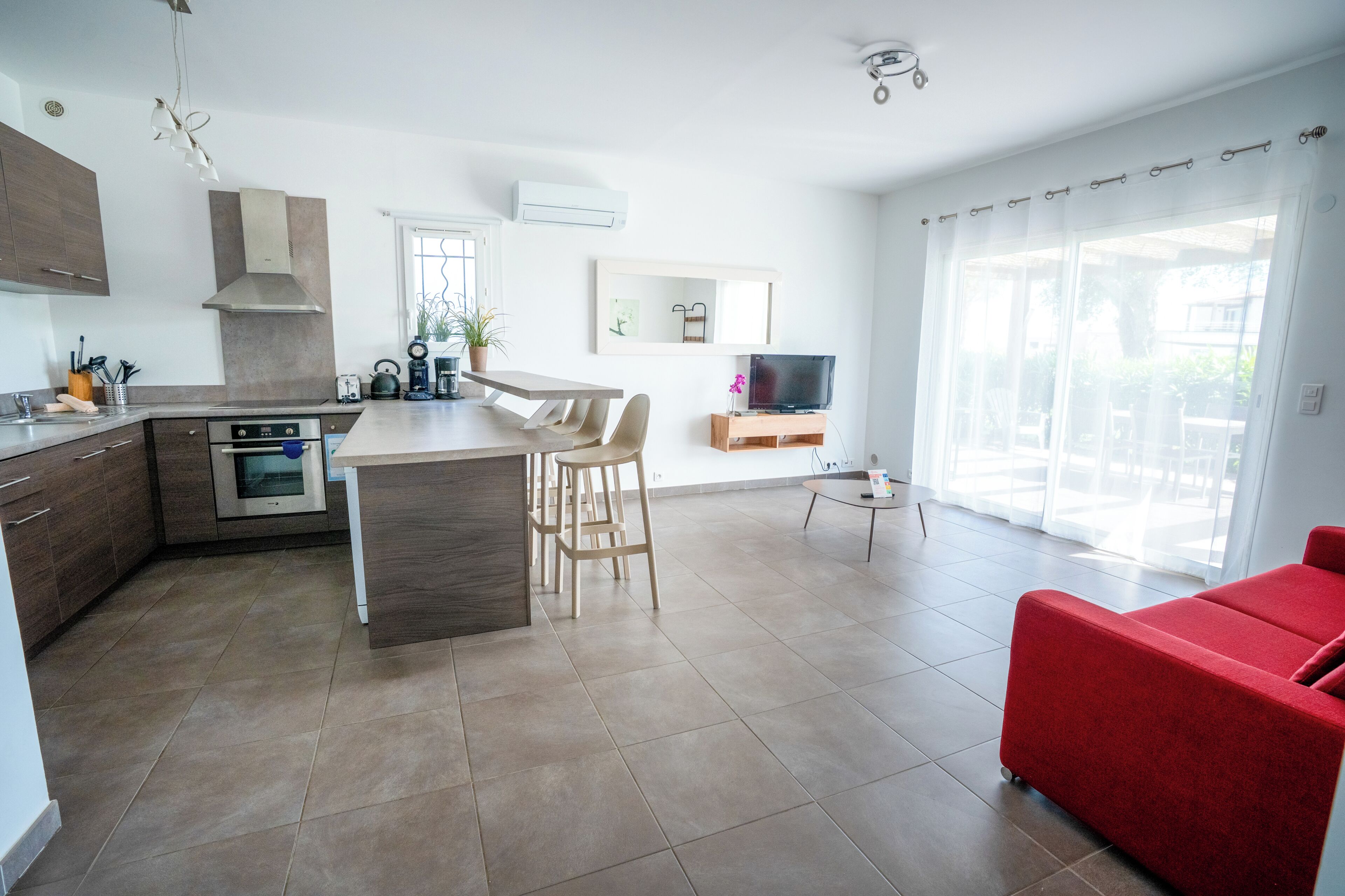 Une cuisine moderne avec un îlot central, un coin repas avec des chaises, un canapé rouge et un téléviseur posé sur un meuble.