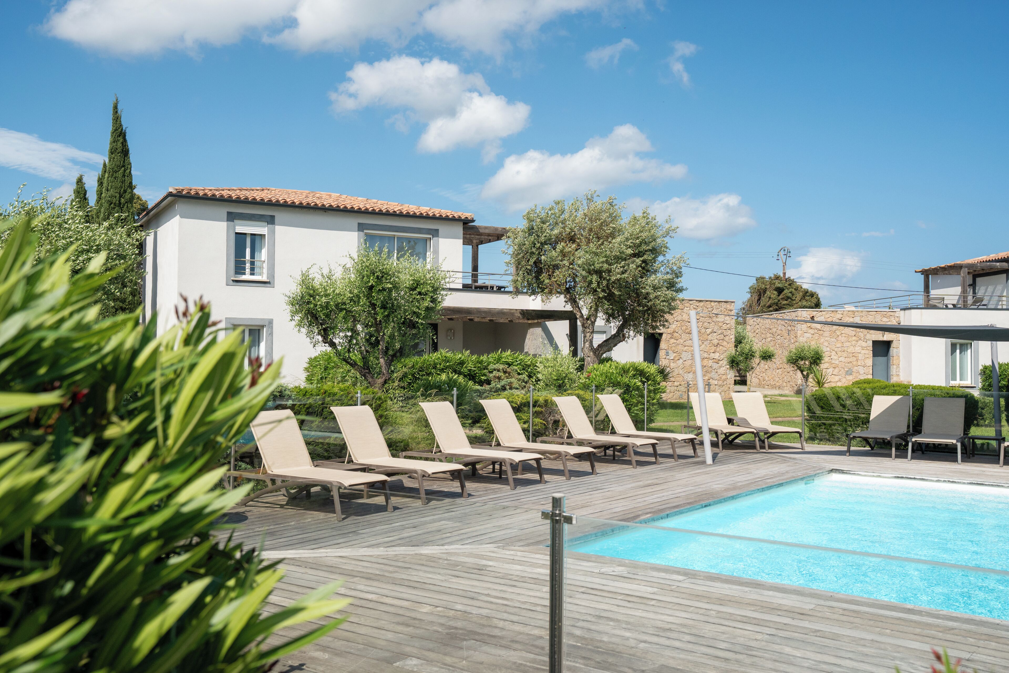 A poolside area with lounge chairs, a swimming pool, and a building with a tiled roof.