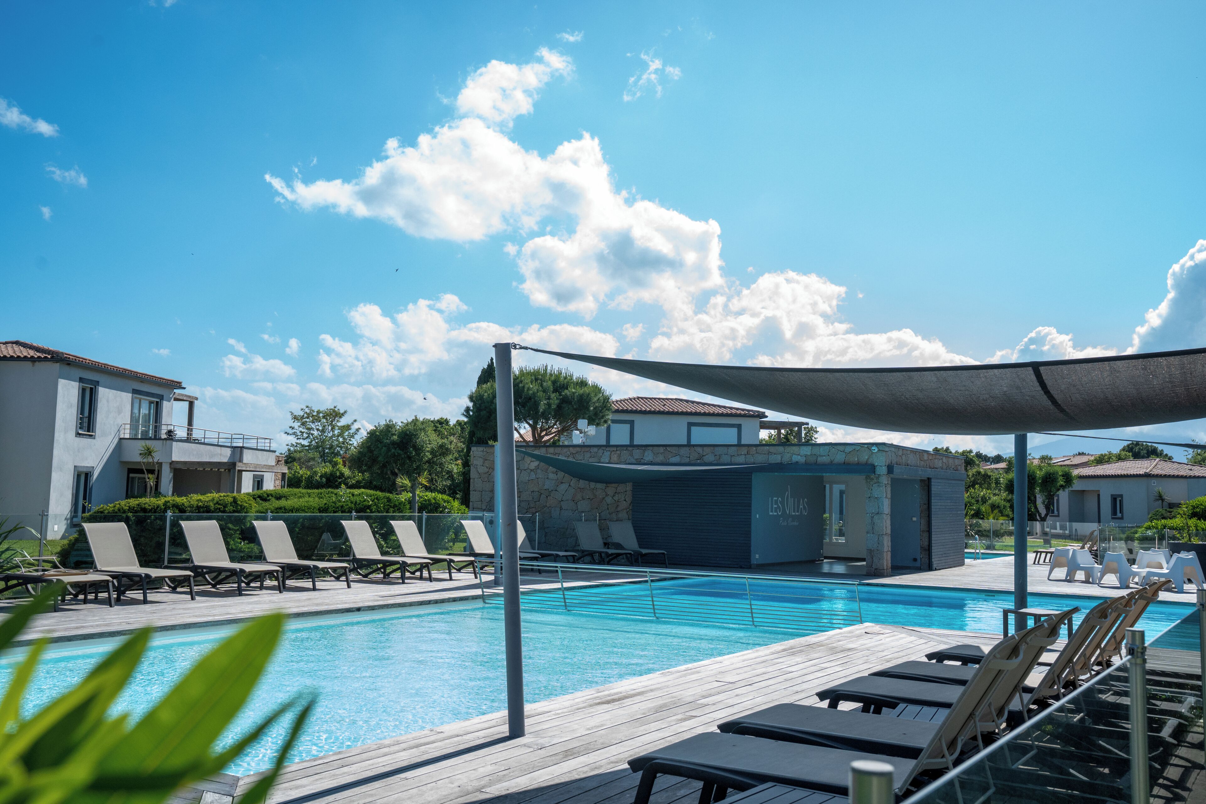 Une piscine avec des chaises longues, un espace ombragé et un bâtiment portant l’inscription « LES VILLAS ».