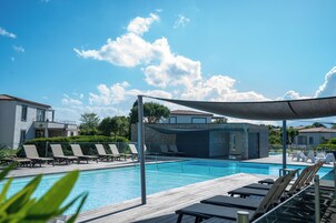 Una piscina con sillas de descanso, una zona sombreada y un edificio que dice 'LES VILLAS'.
