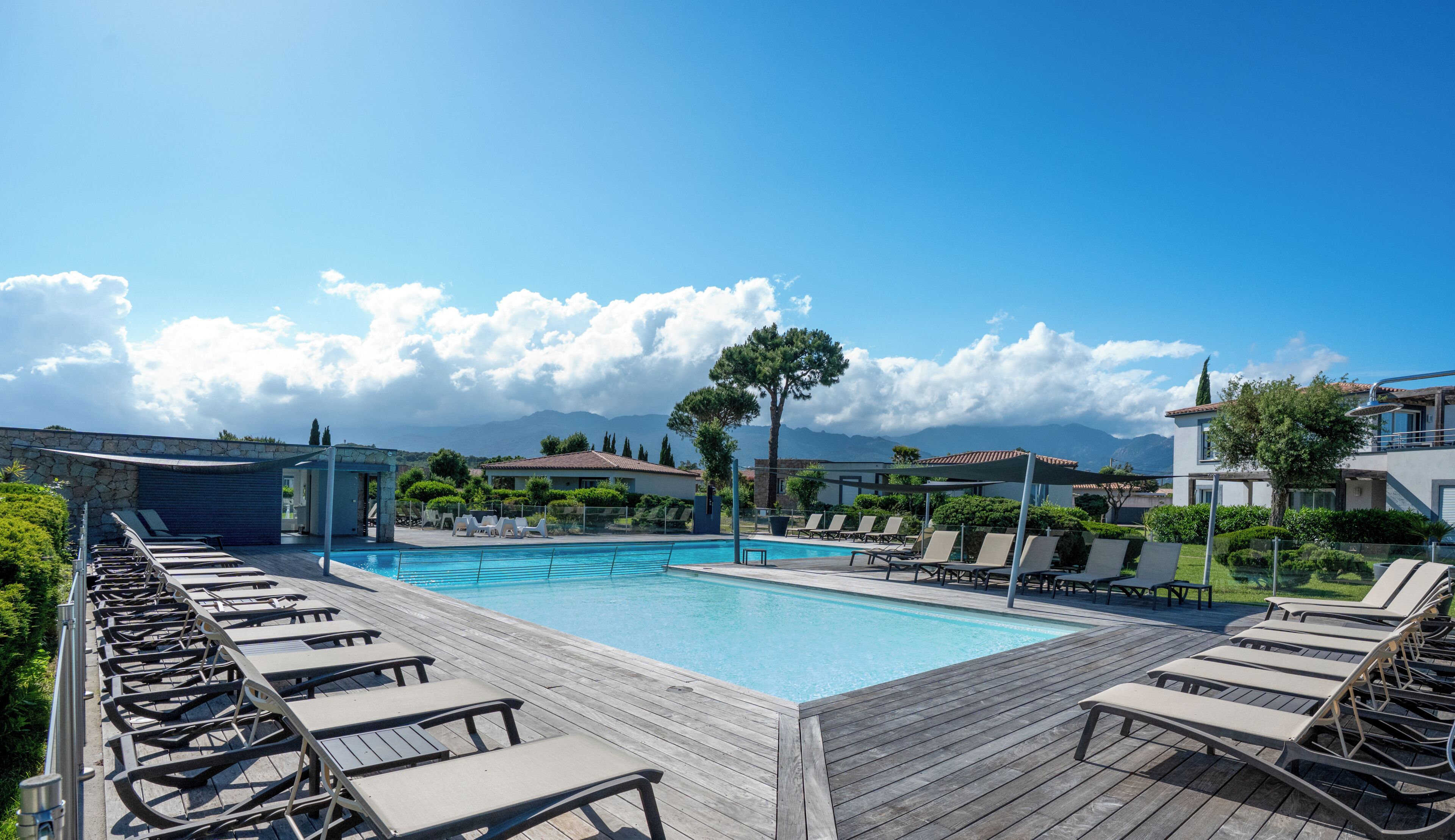 Un espace piscine avec des chaises longues, un ciel dégagé et des montagnes en arrière-plan.
