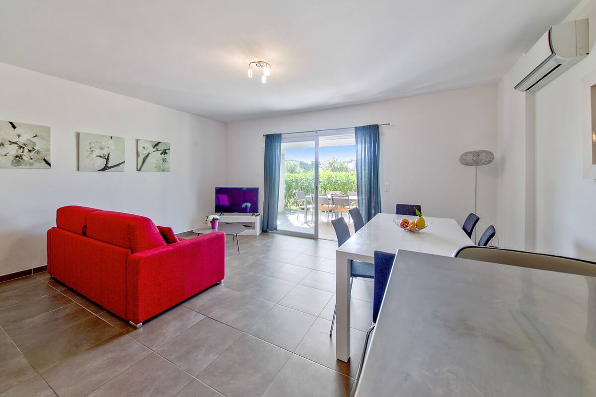 A modern living room with a red sofa, a dining table with chairs, and a TV.