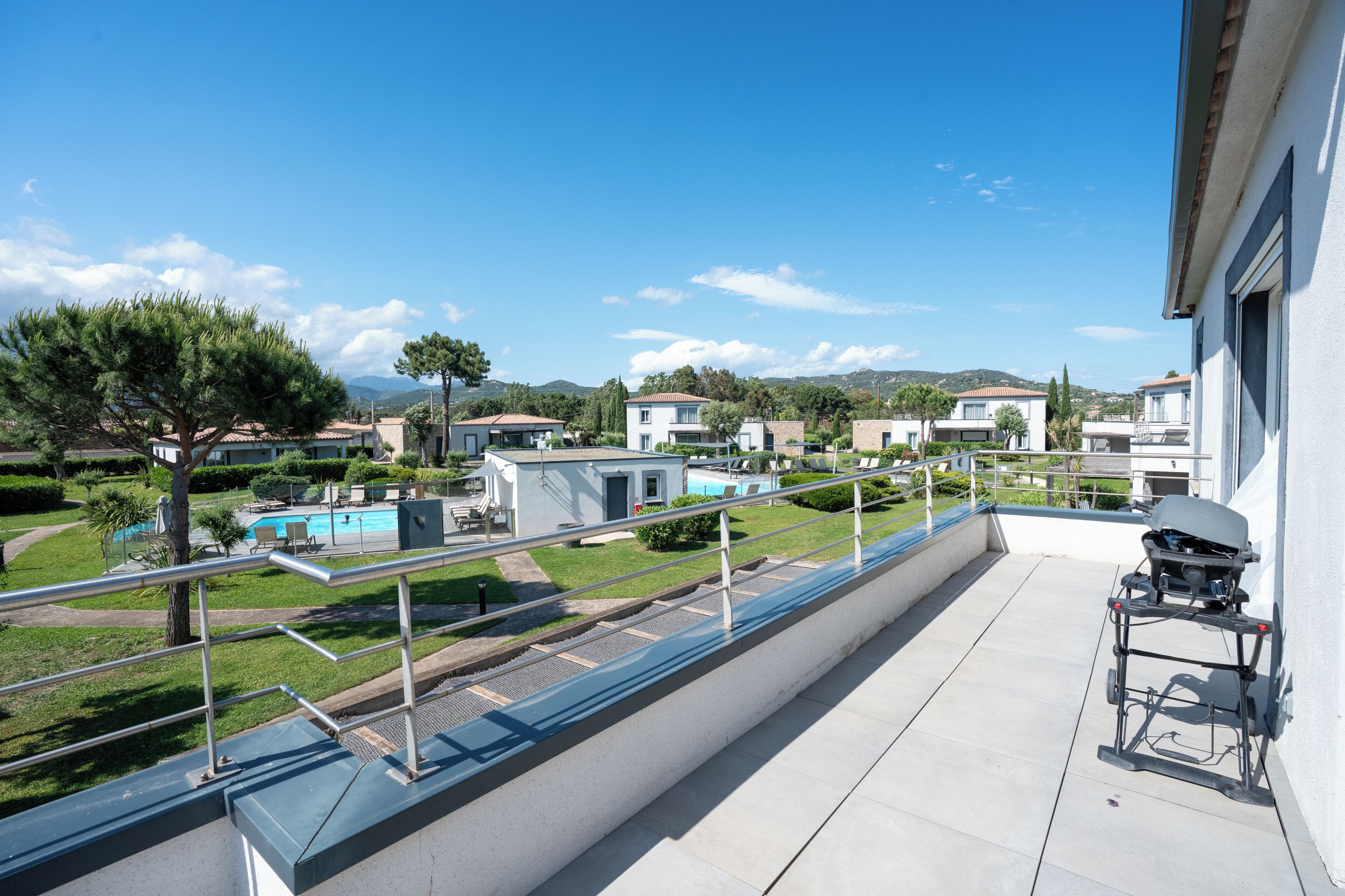 A balcony with a grill, a pool, and a view of other buildings.