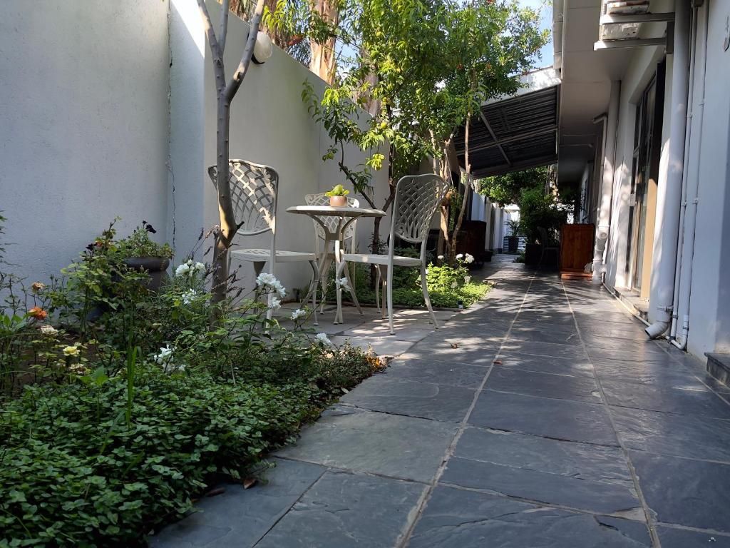 A narrow outdoor corridor with stone flooring, a metal chair, a small table, and potted plants.