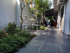A narrow outdoor corridor with stone flooring, a metal chair, a small table, and potted plants. - Border Close Guesthouse (Upington)