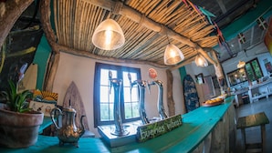 A rustic bar area with wooden beams, a surfboard, and a sign that reads "Buenos Vibes." - Surf Camp San Sebastian Partyhostel (Aia)