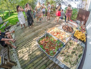 A wooden deck with a variety of food items and a group of people. - Surf Camp San Sebastian Partyhostel (Aia)