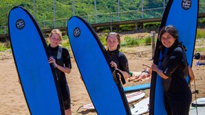 Three people holding surfboards on a beach with a bridge in the background. - Surf Camp San Sebastian Partyhostel (Aia)