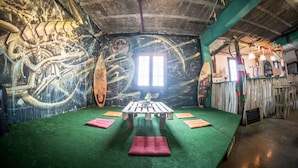 A room with a mural, a table, and green flooring. - Surf Camp San Sebastian Partyhostel (Aia)