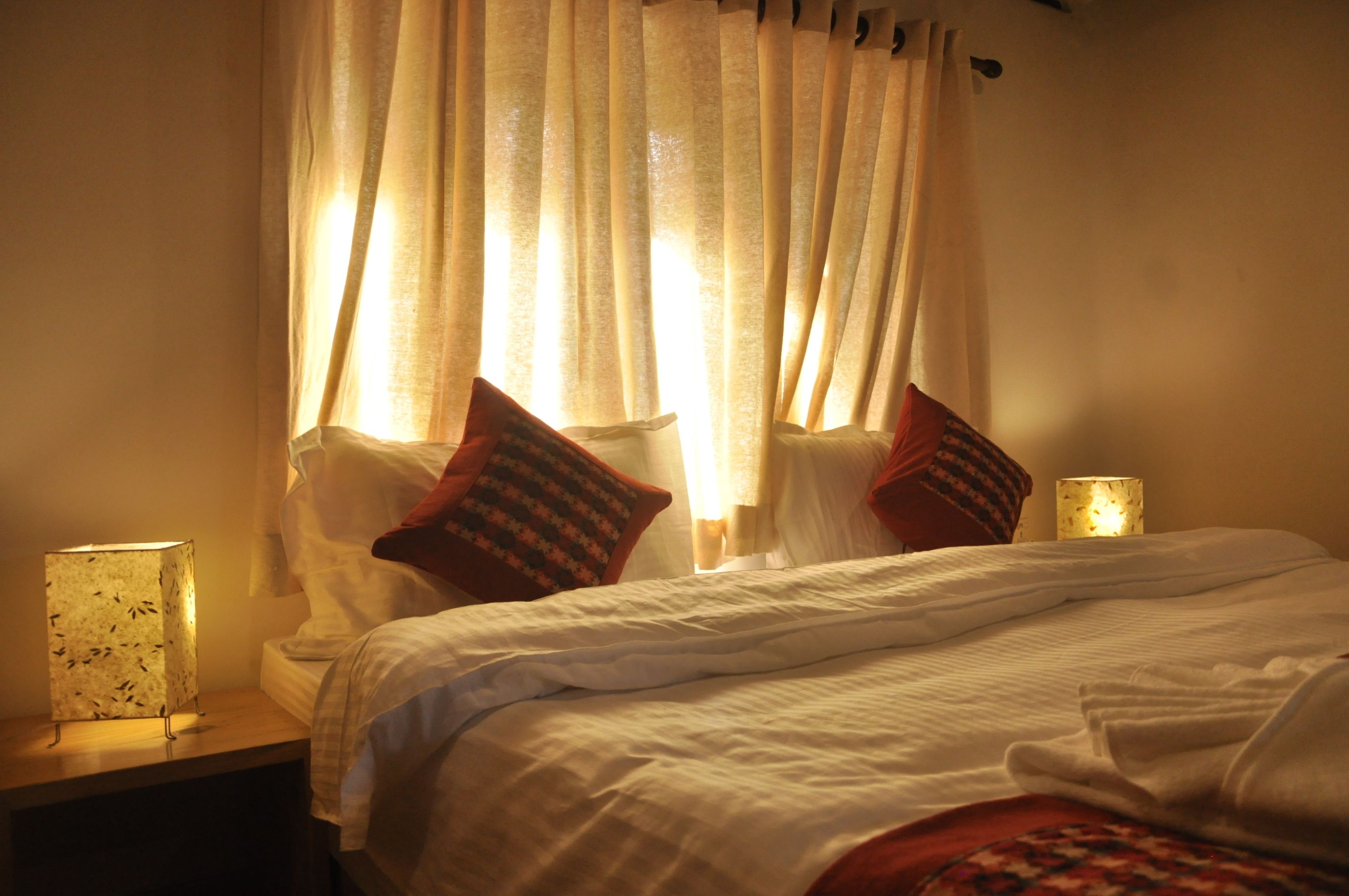 A neatly made bed with white linens, two pillows, and a bedside lamp on a wooden nightstand.