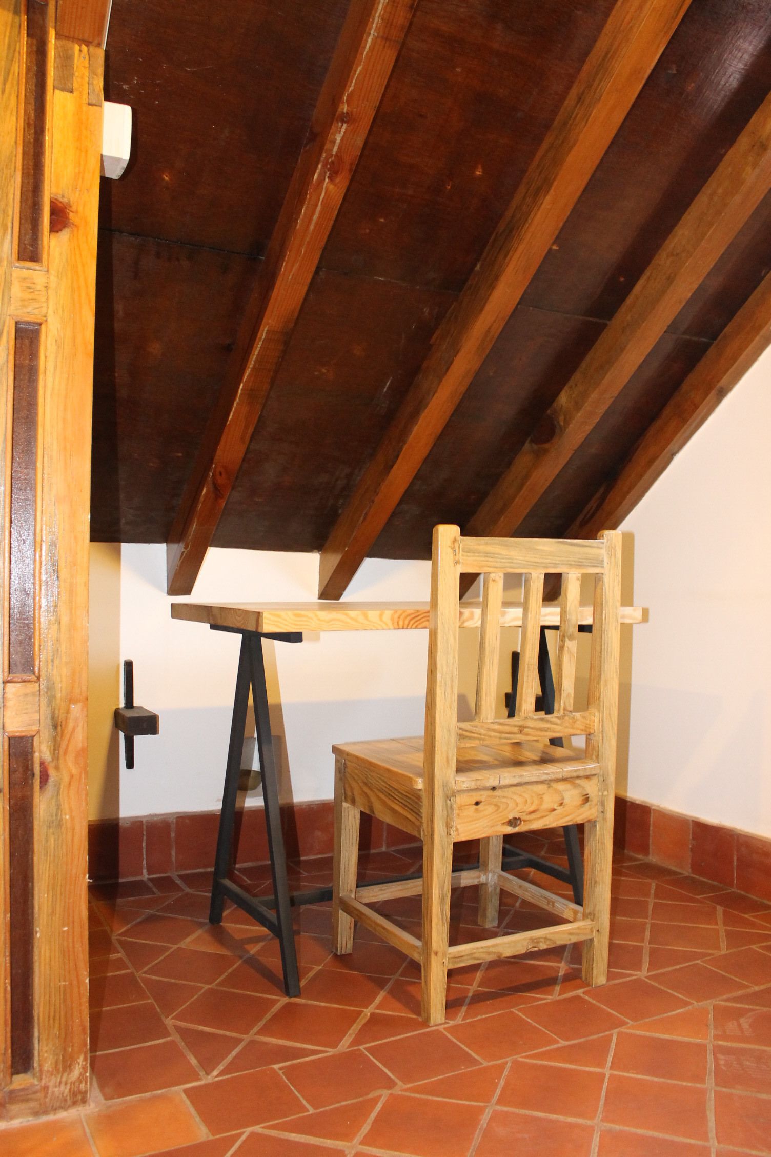 A rustic wooden chair and table in a room with exposed wooden beams and terracotta tiles.