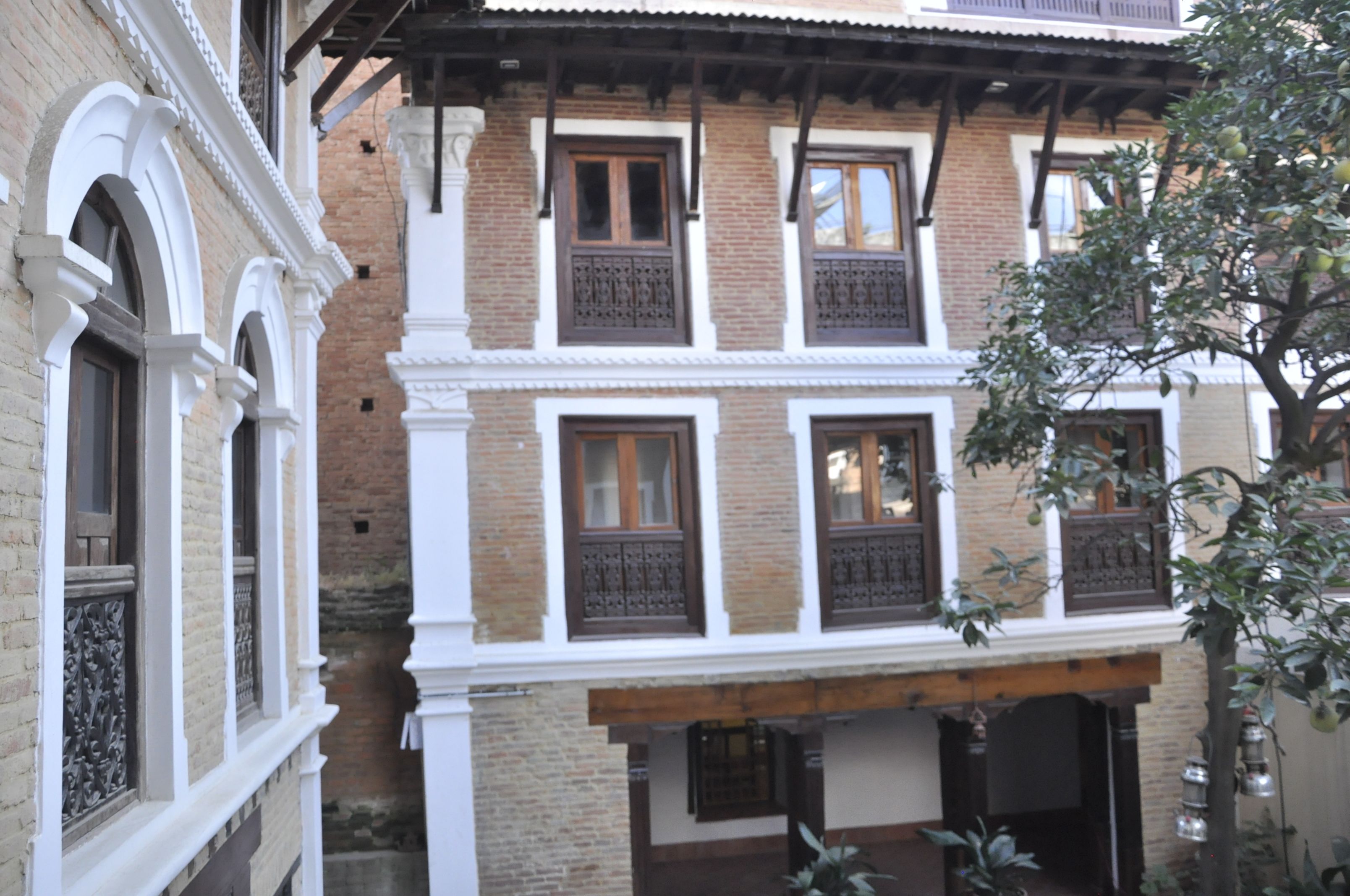 A traditional building with multiple windows and balconies, featuring brick and white walls, and a tree in the foreground.
