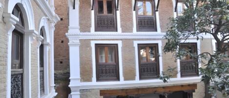 A traditional building with multiple windows and balconies, featuring brick and white walls, and a tree in the foreground.