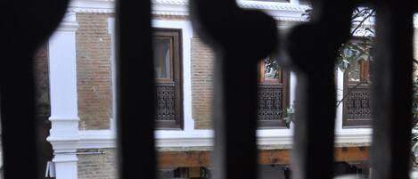 Vista a través de elaboradas rejas de hierro de un edificio con múltiples ventanas y un patio empedrado.