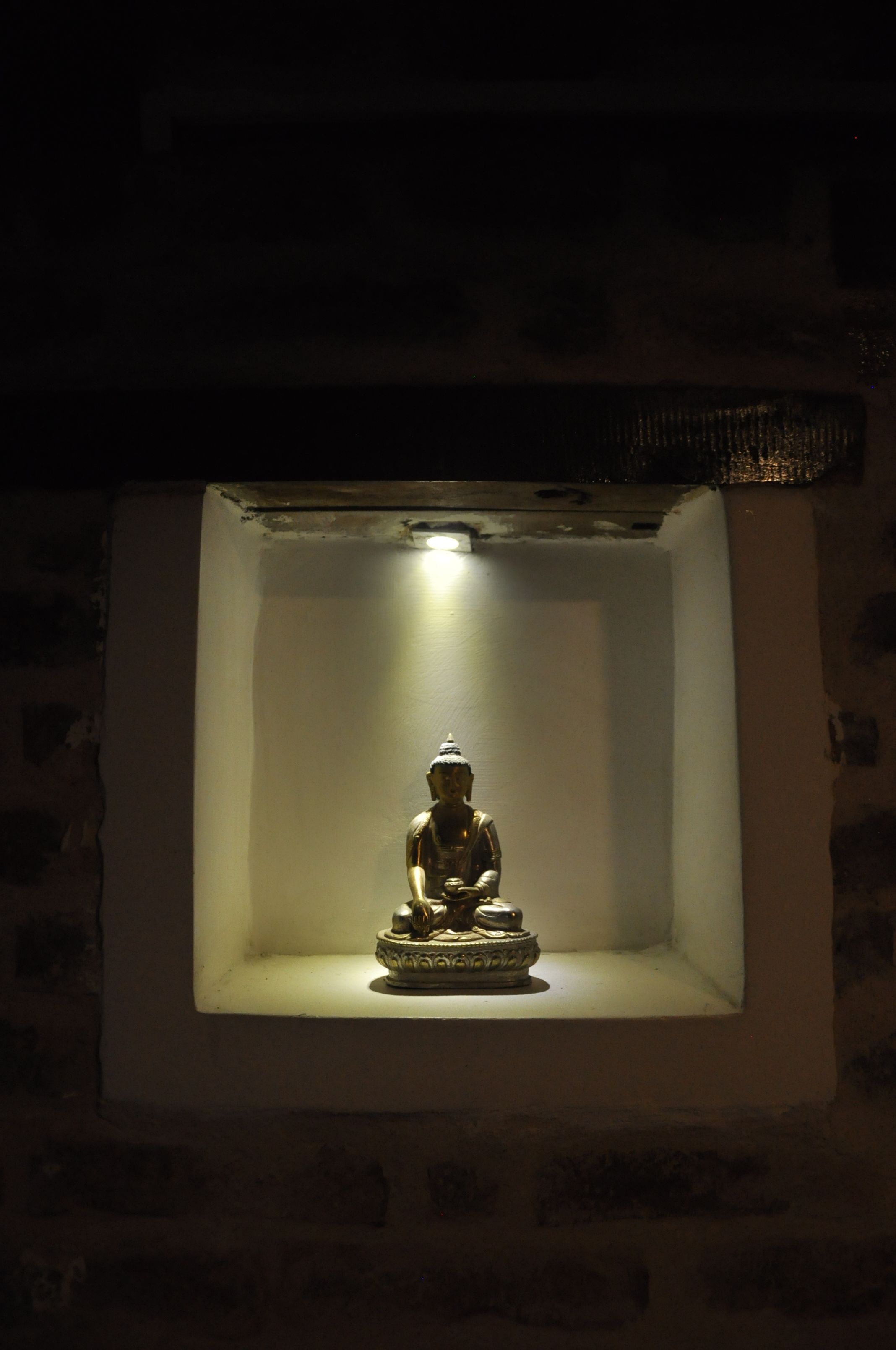 A statue in a well-lit alcove with a stone wall background.