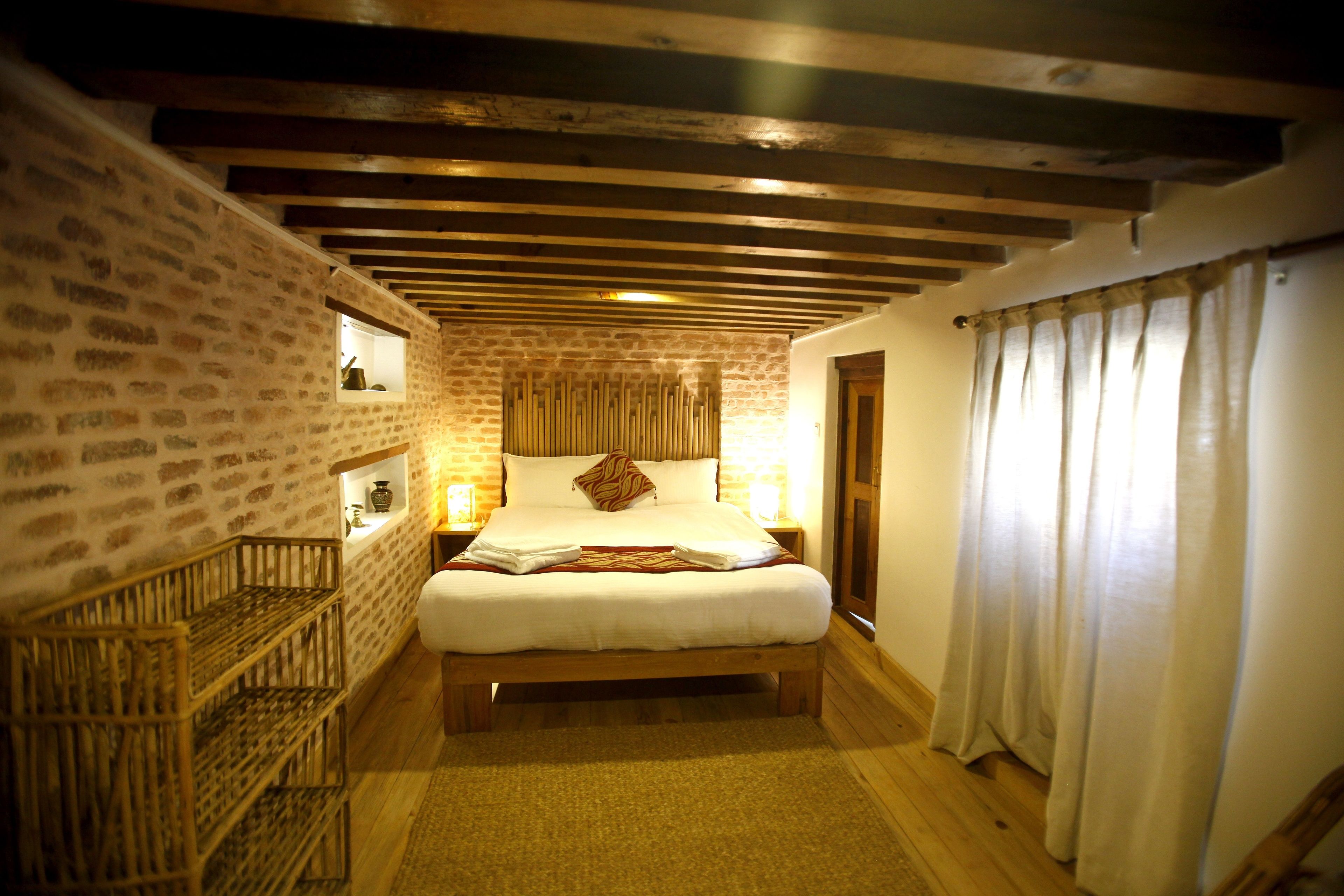 A bedroom with a wooden bed, brick walls, a wooden ceiling, and a window with curtains.