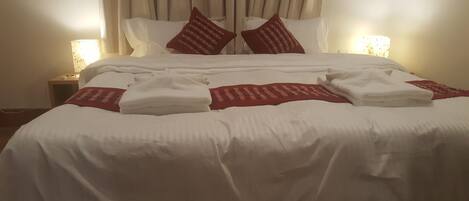 A neatly made bed with white linens and red patterned pillows, a folded red blanket, and two bedside lamps on a nightstand.
