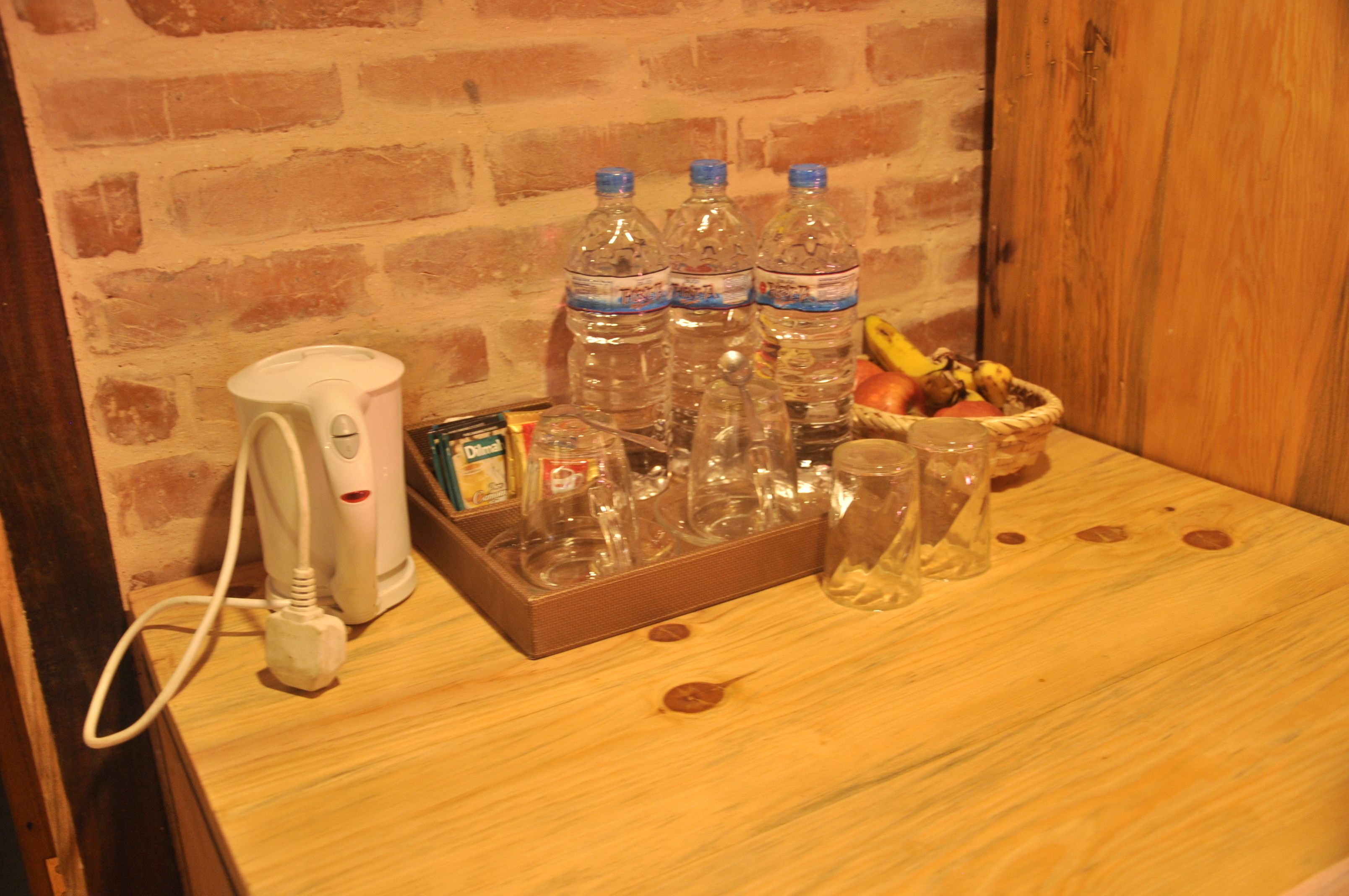 A wooden table with a coffee maker, water bottles, glasses, and a fruit basket.