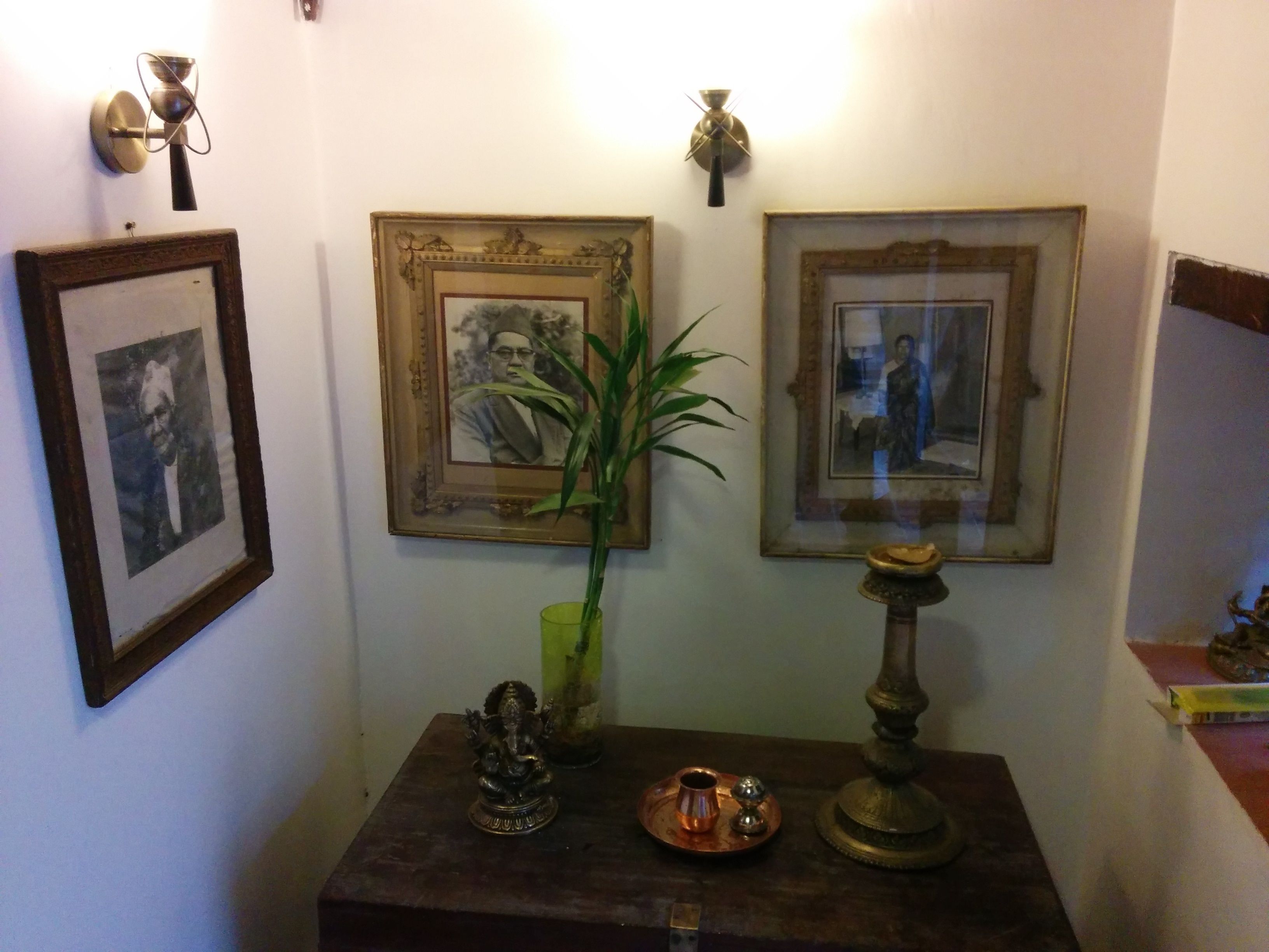 Una habitación con una mesa de madera oscura, un jarrón verde con una planta y tres cuadros en la pared.
