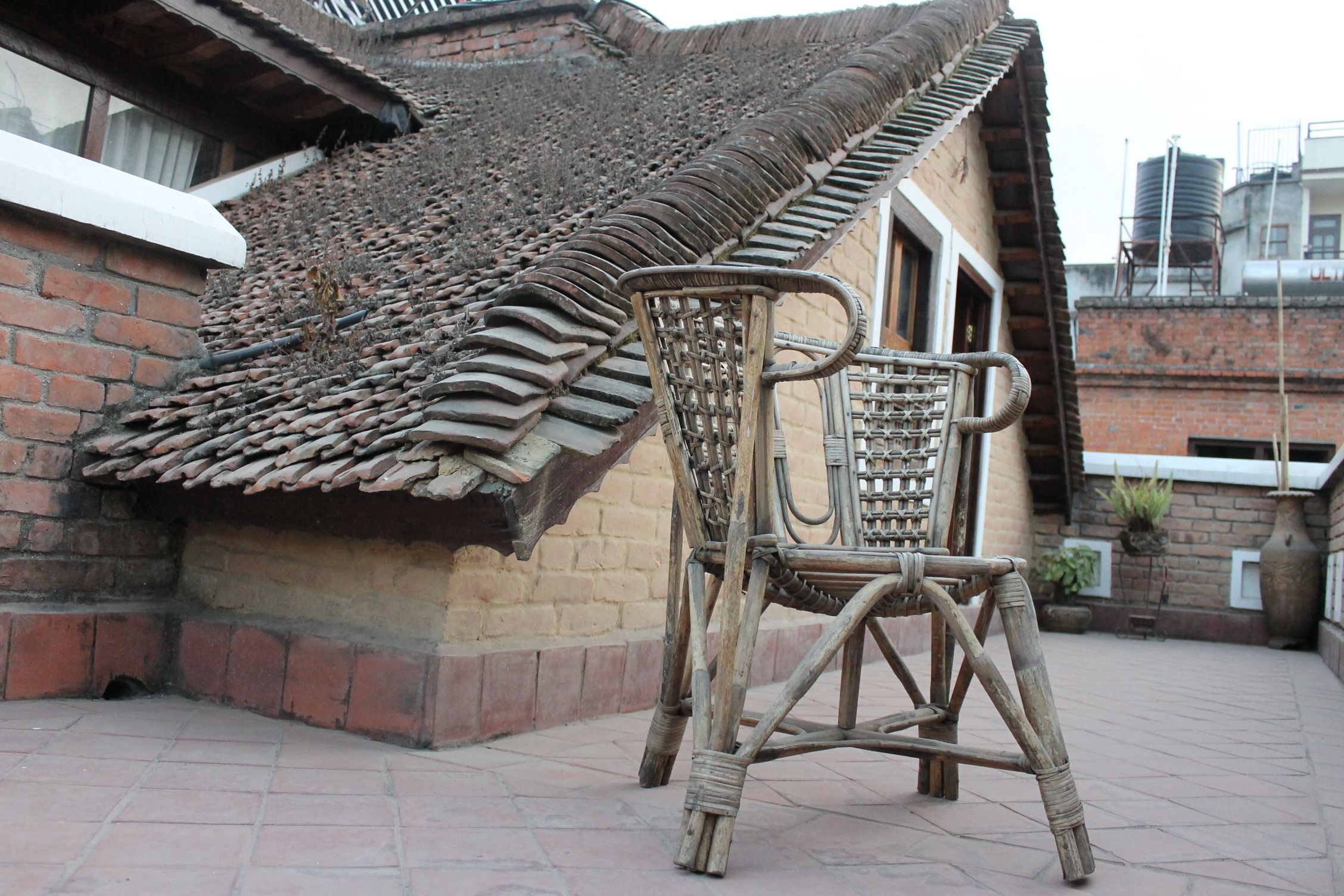 A traditional building with a tiled roof and a brick wall. A wicker chair is placed in front of the building.