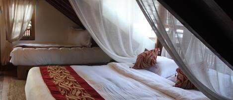 A bedroom with two beds, each covered with white linens and a red decorative border. The room has a sloped ceiling and a window with curtains.