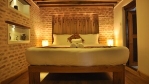 Un dormitorio con pared de piedra, estructura de cama de madera y lámparas de noche.
