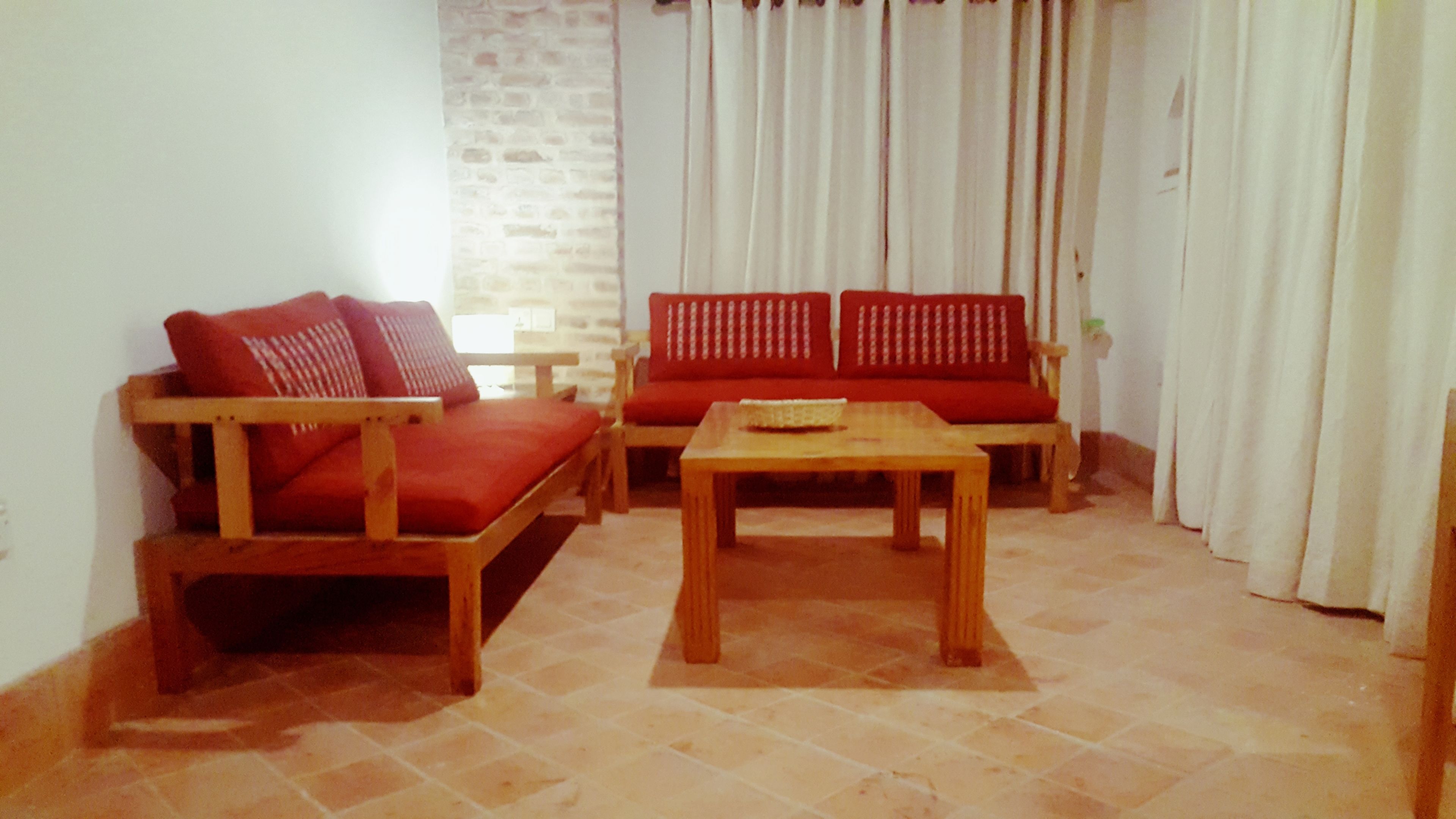 A living room with two wooden sofas, a wooden coffee table, and a stone-tiled floor.