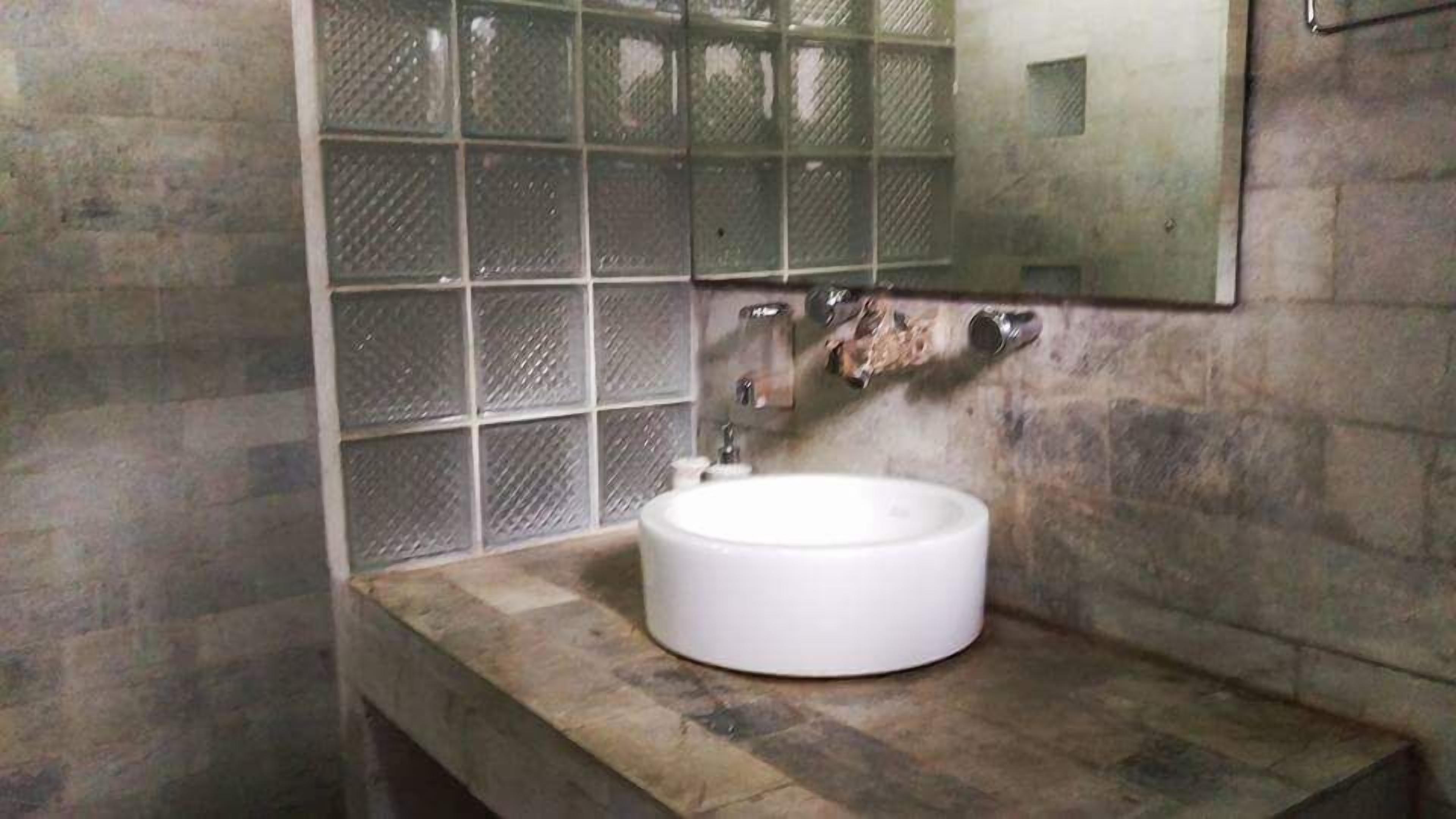 A bathroom with a round white sink, a mirror, and a tiled wall.