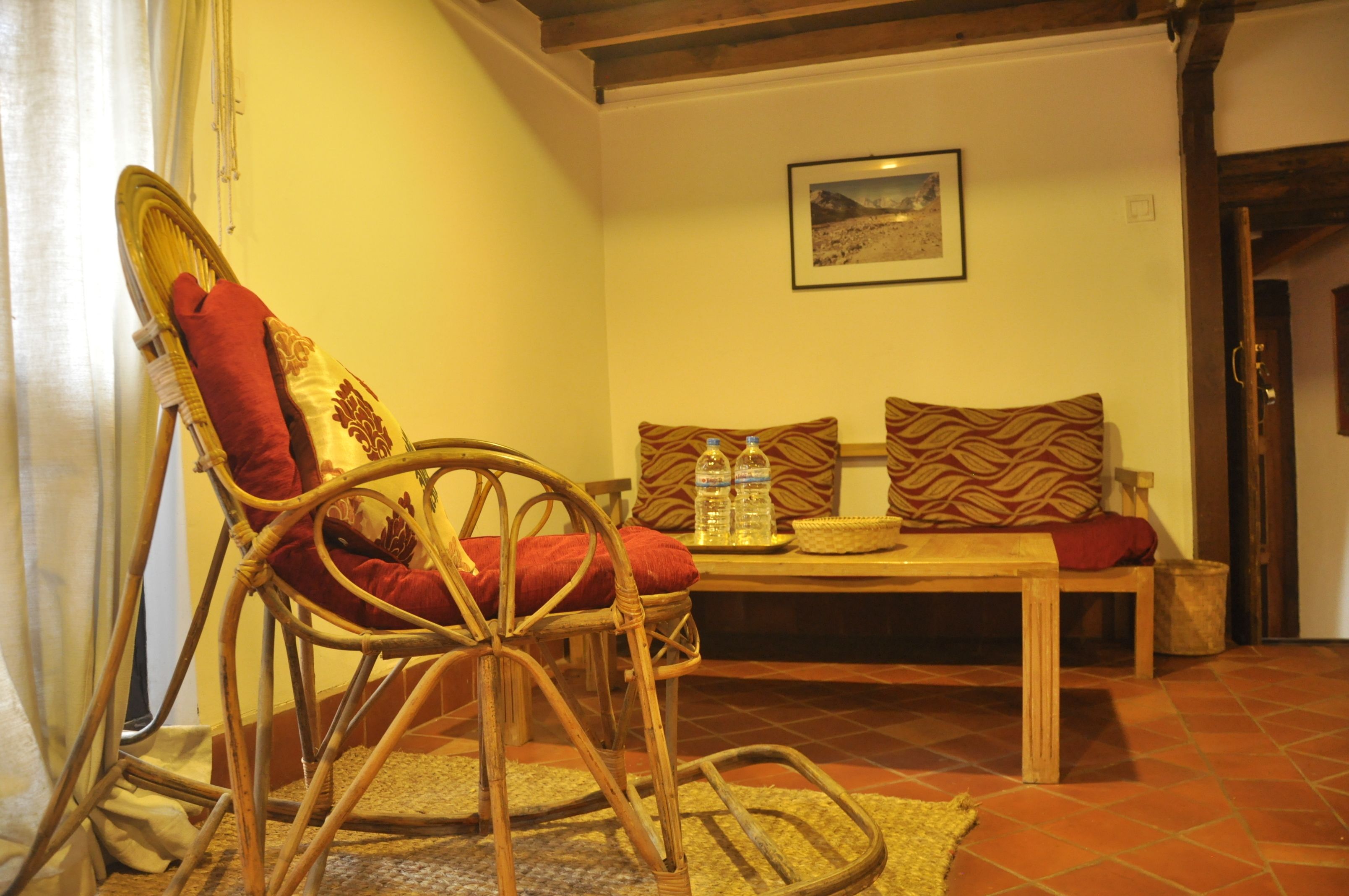Une pièce comprenant une chaise en osier, un banc en bois et une table avec deux coussins et une bouteille d’eau.