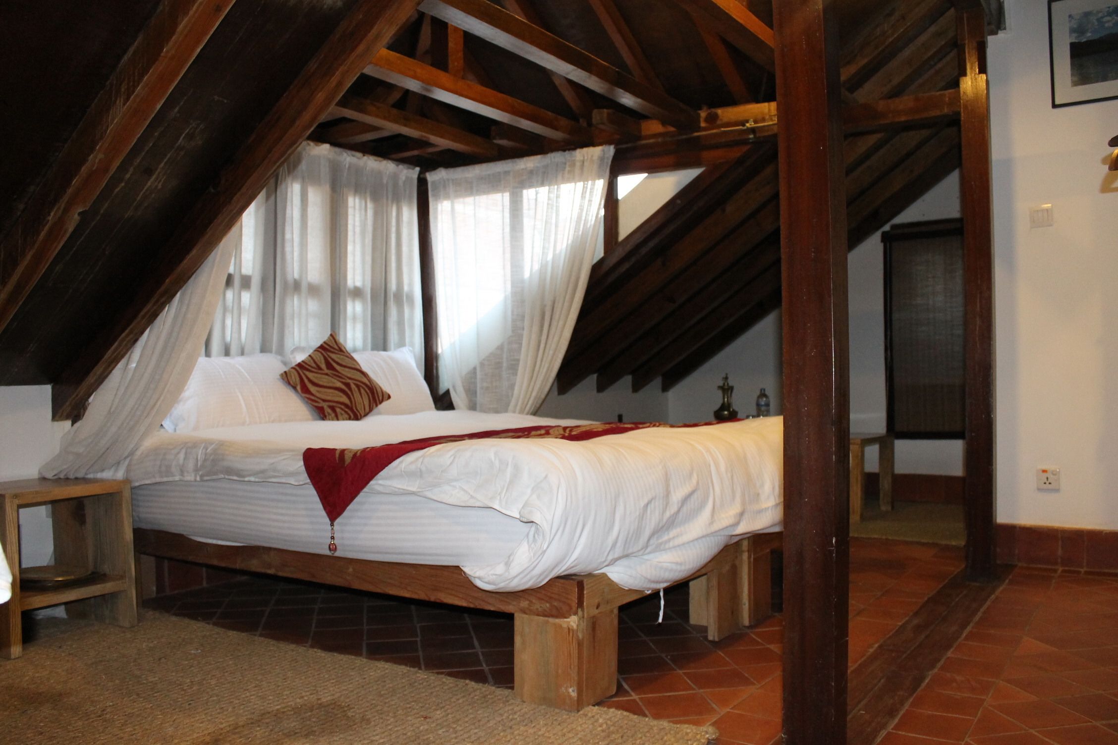 A bedroom with a wooden bed, white linens, a red throw blanket, and a wooden ceiling structure.