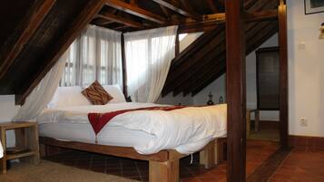 A bedroom with a wooden bed, white linens, a red throw blanket, and a wooden ceiling structure.