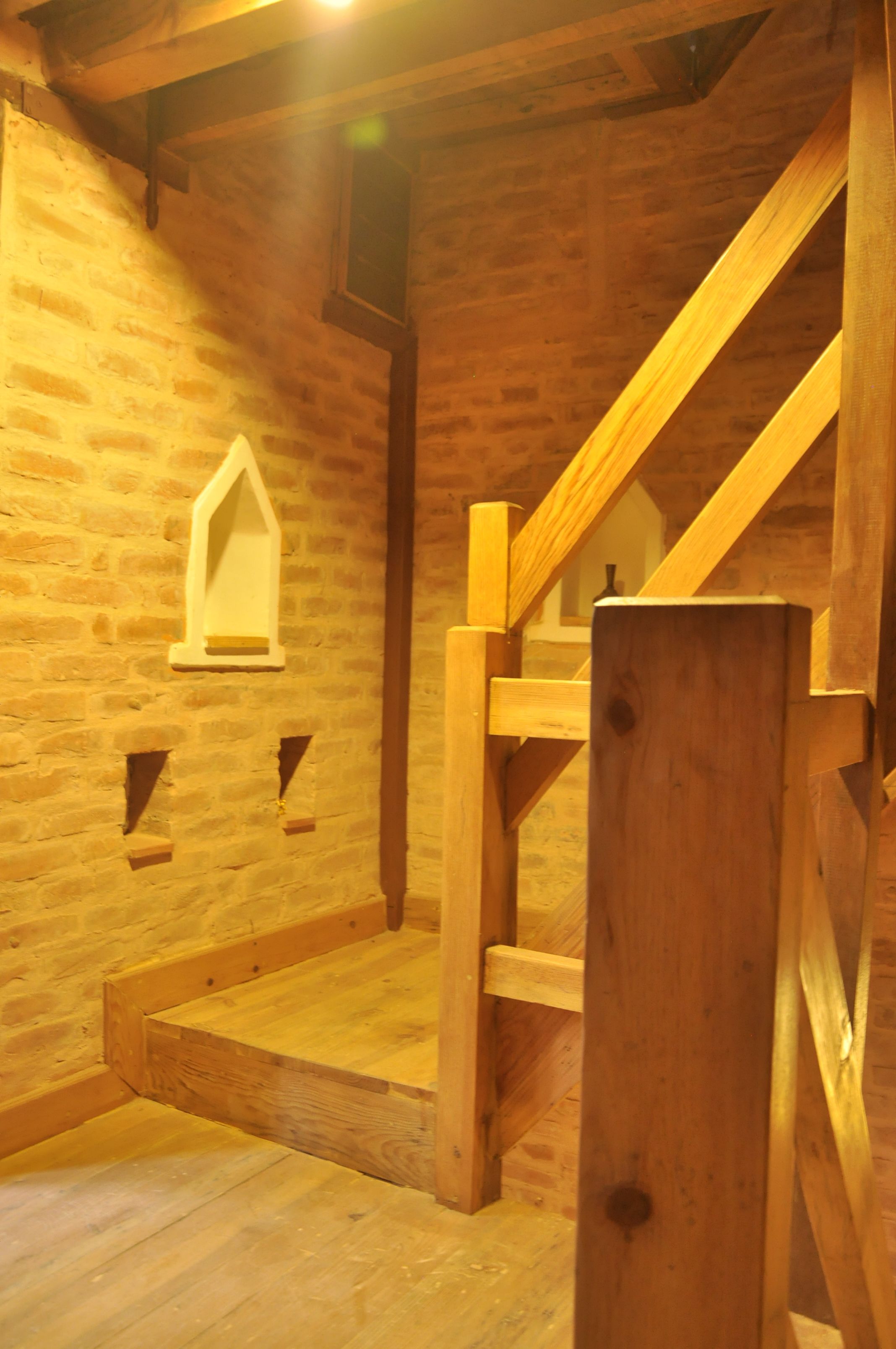 A wooden staircase leading to a loft area with exposed brick walls and a wooden floor.