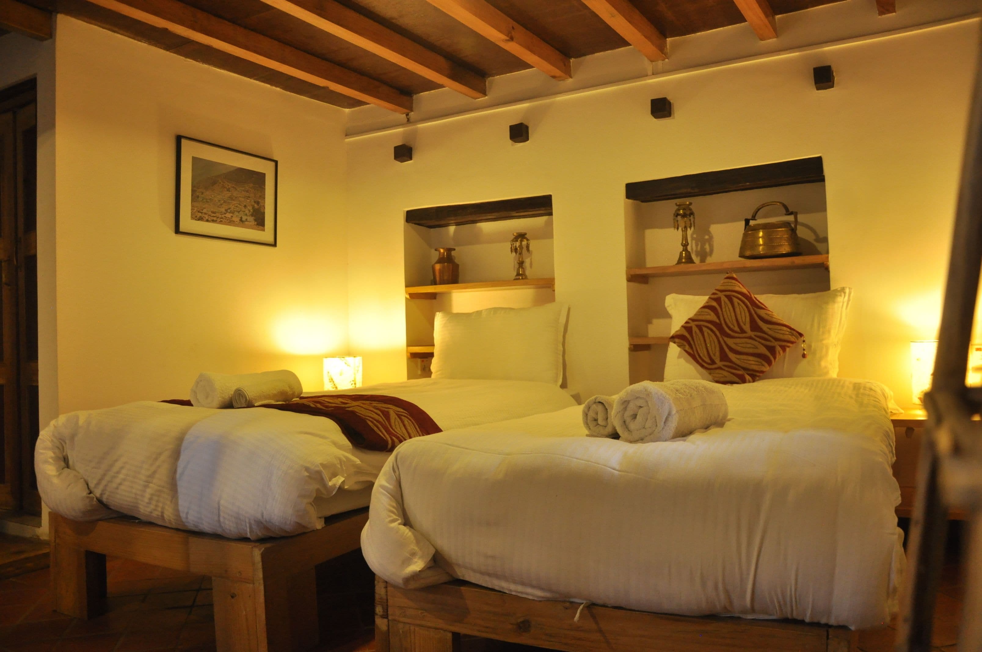 A hotel room with two beds, wooden headboards, a wooden bench, and built-in shelves with decorative items.