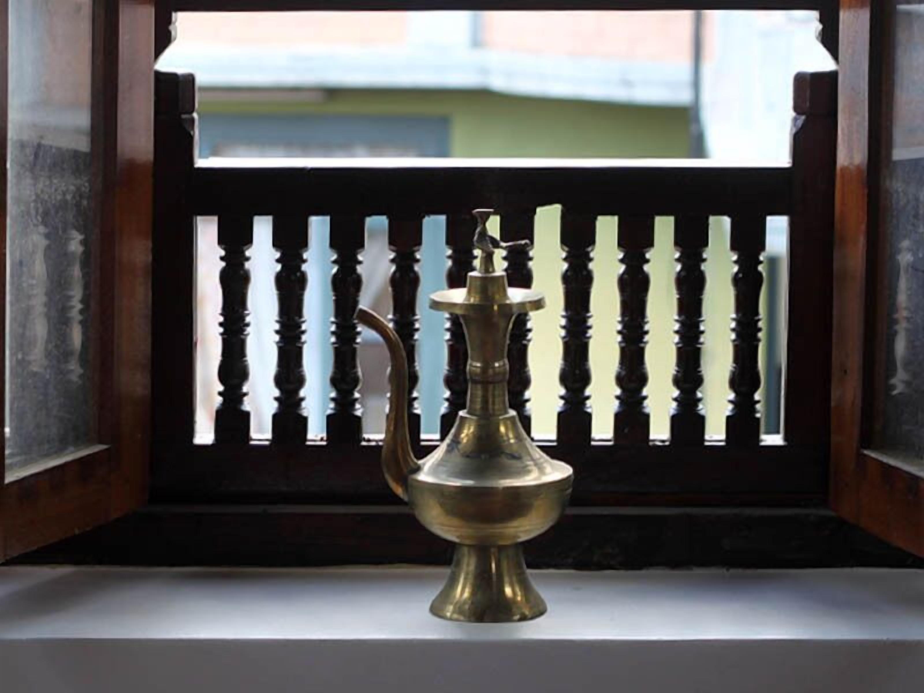 Un dispensador de agua de bronce en una ventana con barandilla de madera.