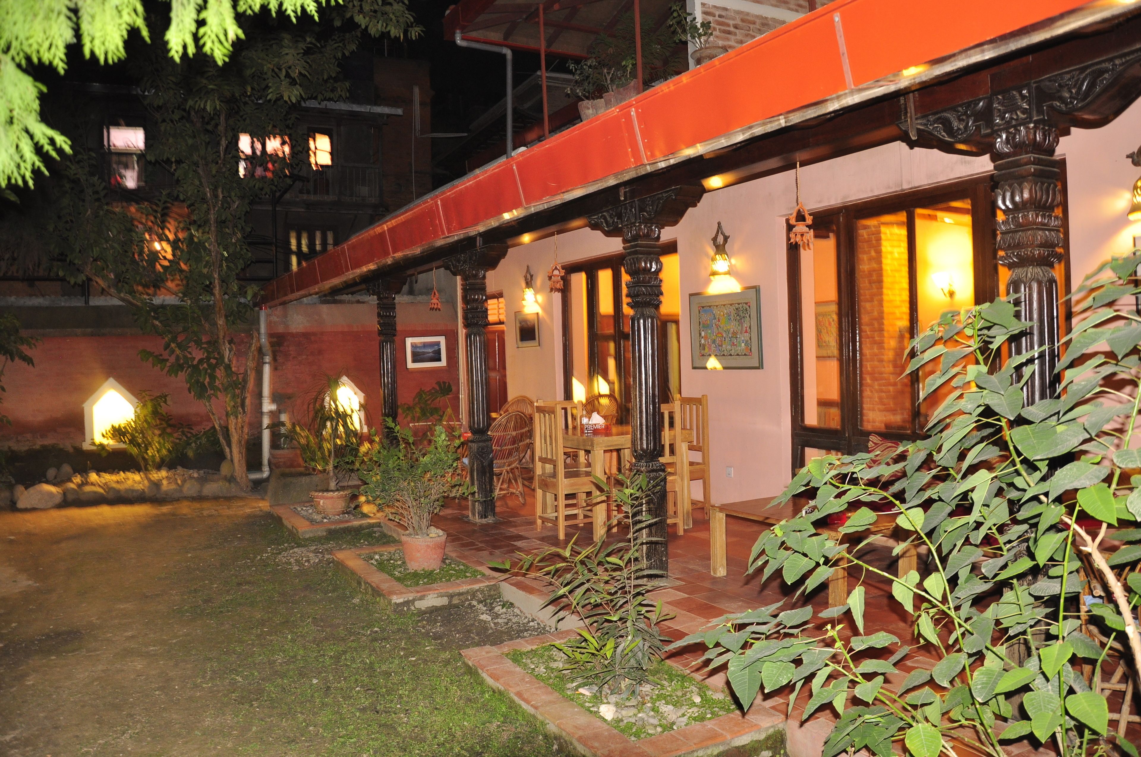 A building with a covered outdoor seating area, potted plants, and a brick wall.