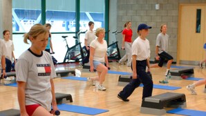 A group of people exercising on step platforms in a gym with wooden floors and large windows. - The Quigley Residence (Garraun)