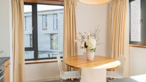 A modern room with a round wooden table, white chairs, a vase with white flowers, and a window with curtains. - The Quigley Residence (Garraun)